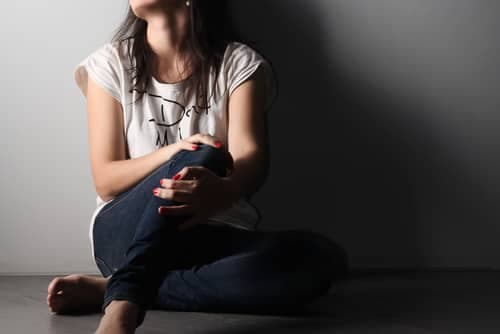young adult sitting against grey wall struggling with addiction
