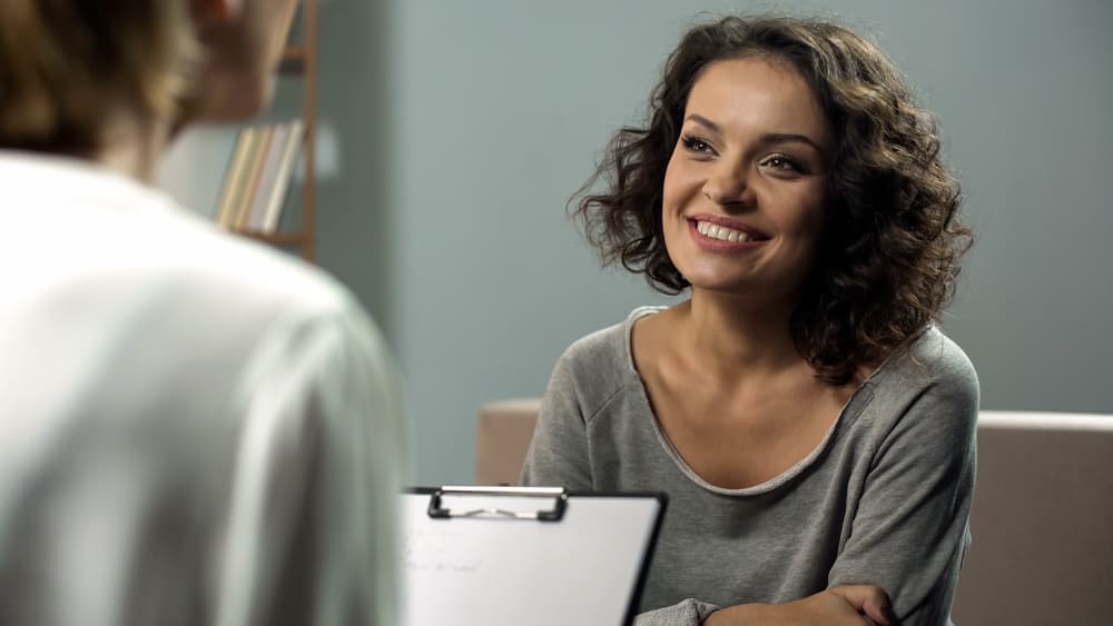 Woman smiling while sitting across from addiction treatment clinician