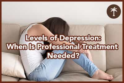 Depressed young woman sitting on sofa embracing knees with hands.